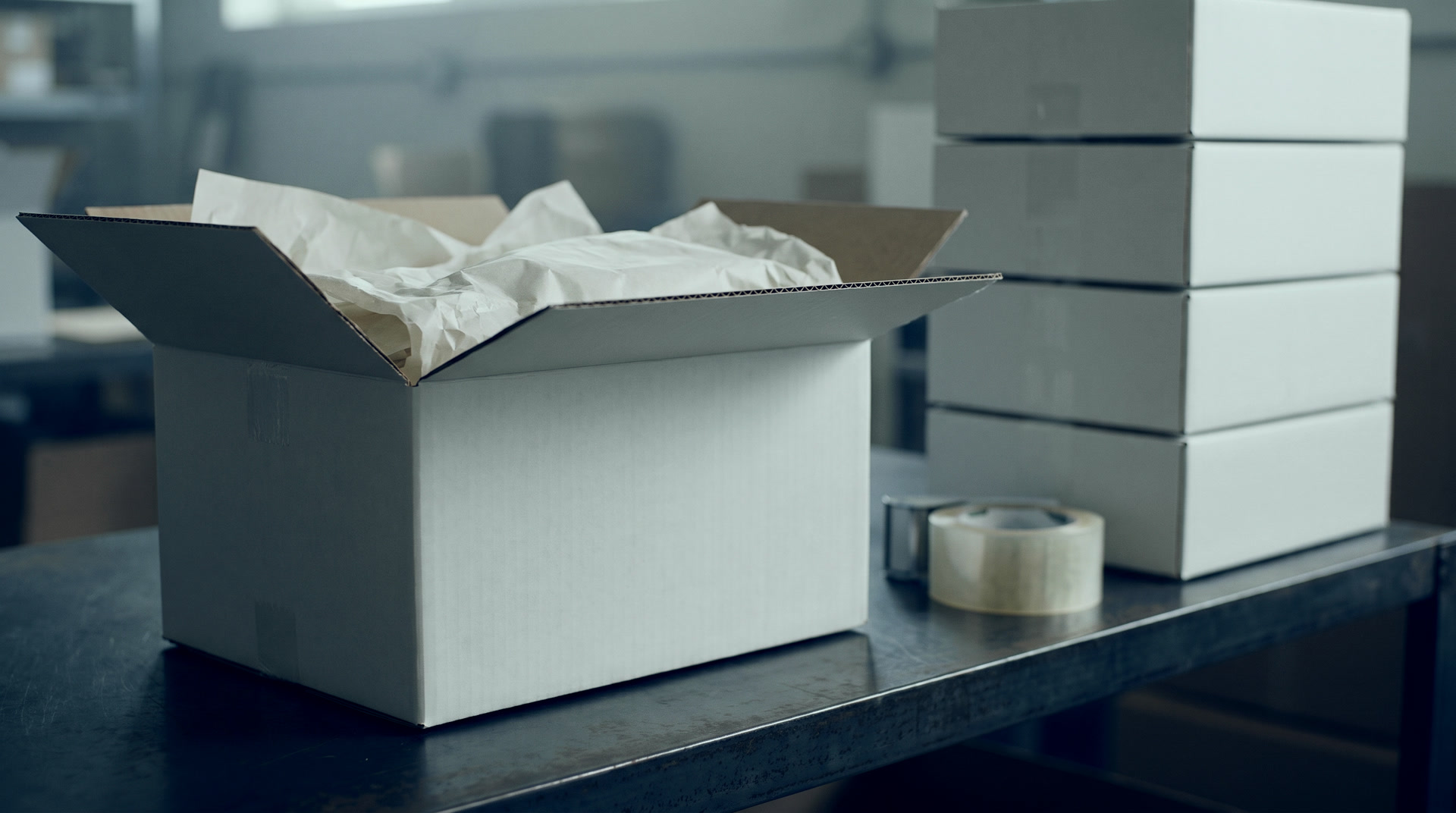 A plain white shipping box open on a packing bench in a cold blue-lit warehouse